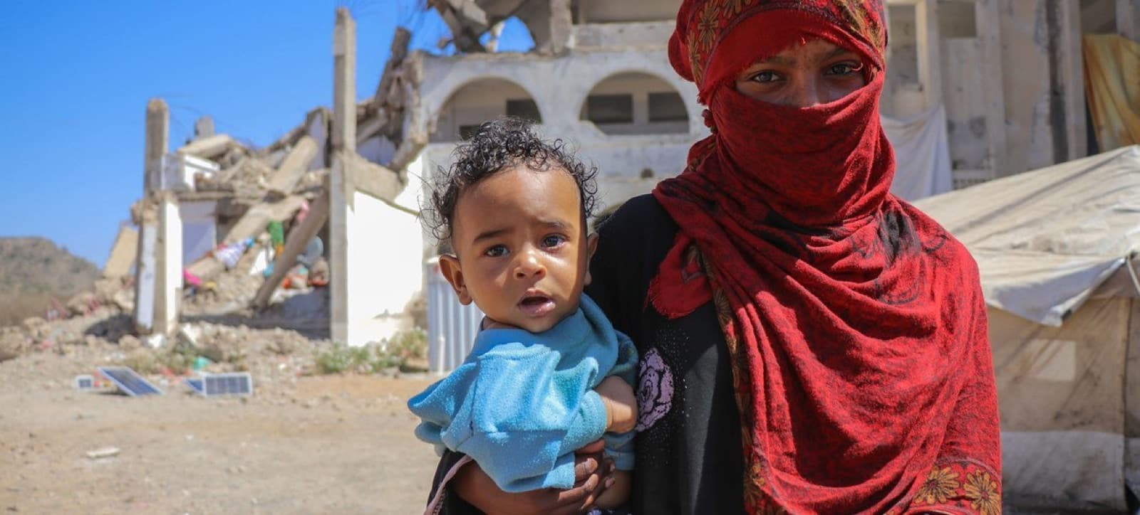 A mother holding her child in front of a destroyed building